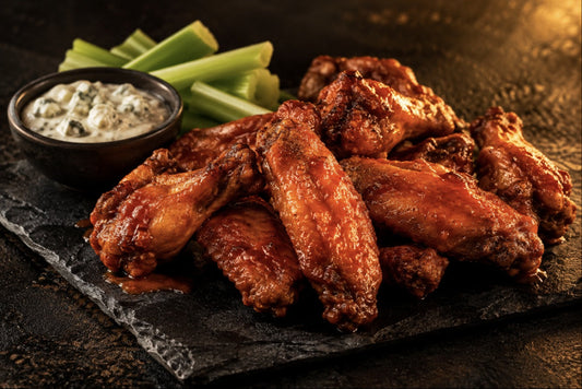Crispy buffalo wings tossed in red hot sauce with blue cheese dip and celery on black stone